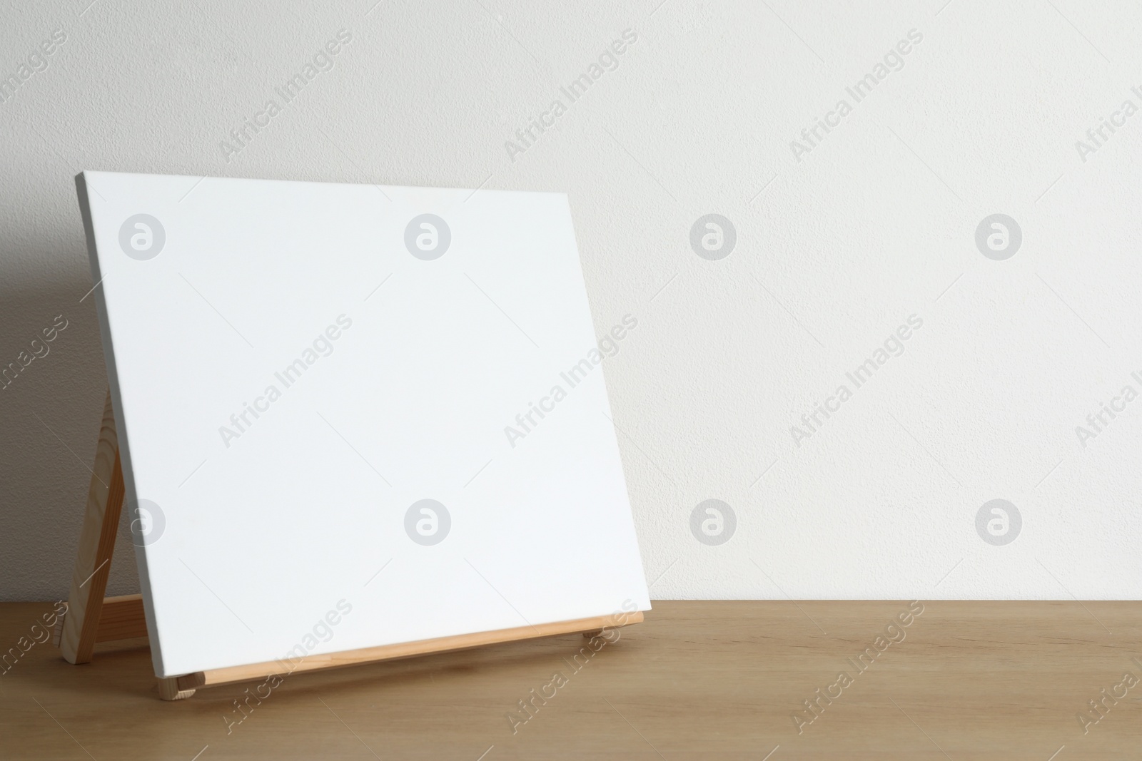 Photo of Wooden easel with blank canvas on table. Space for text