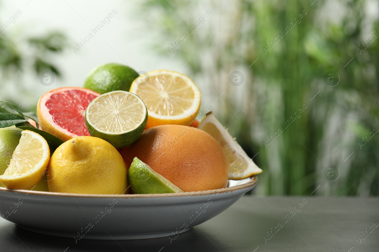 Photo of Different fresh citrus fruits on grey table against blurred background, closeup. Space for text