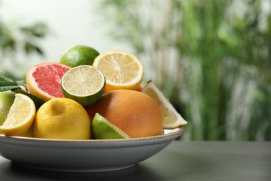 Photo of Different fresh citrus fruits on grey table against blurred background, closeup. Space for text