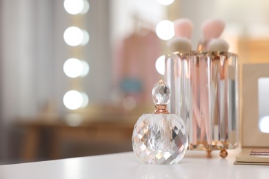 Bottle of perfume on white table in makeup room, space for text