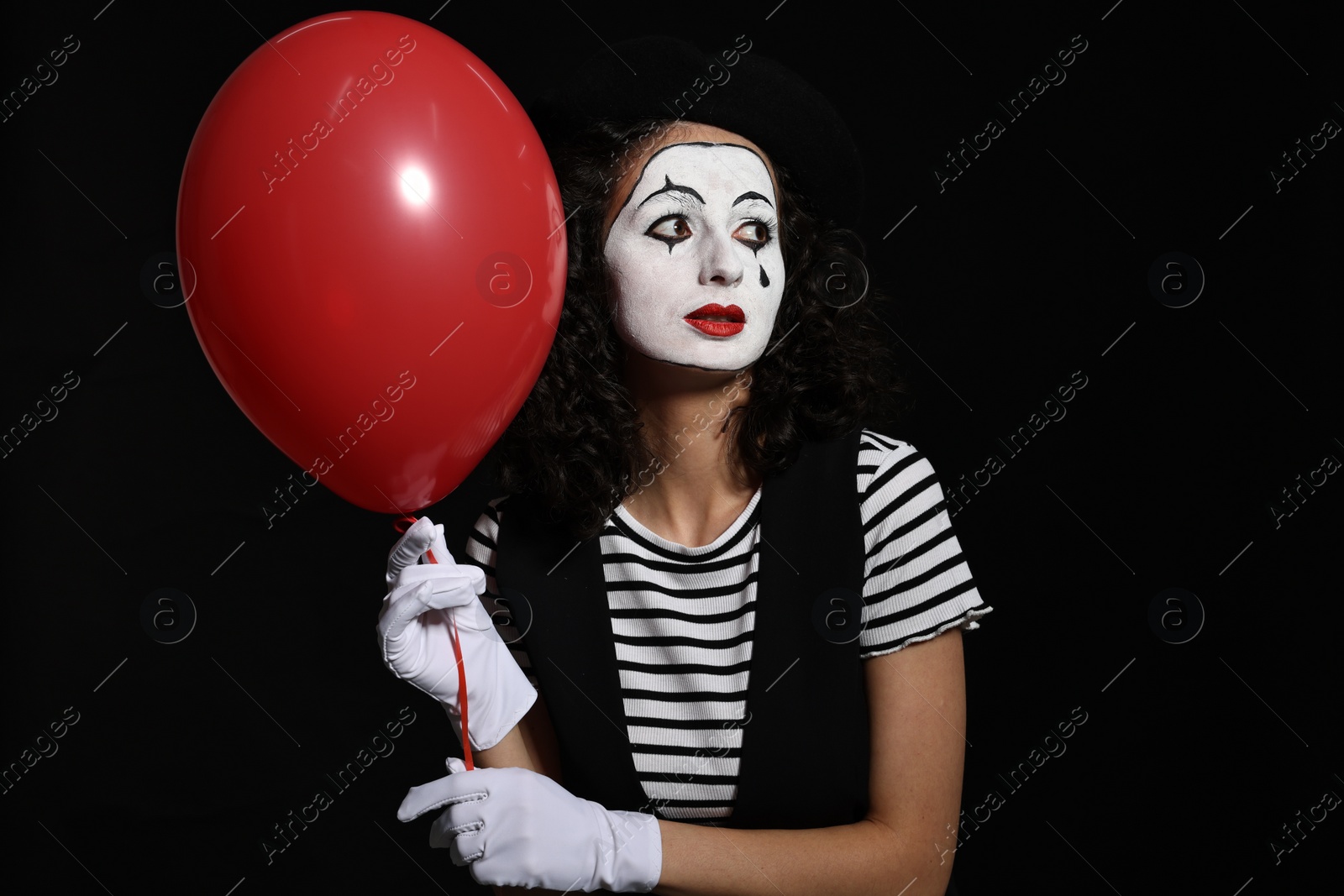 Photo of Young woman in mime costume with balloon posing on black background