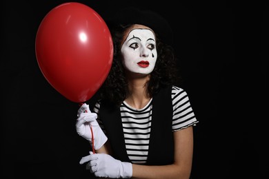 Young woman in mime costume with balloon posing on black background