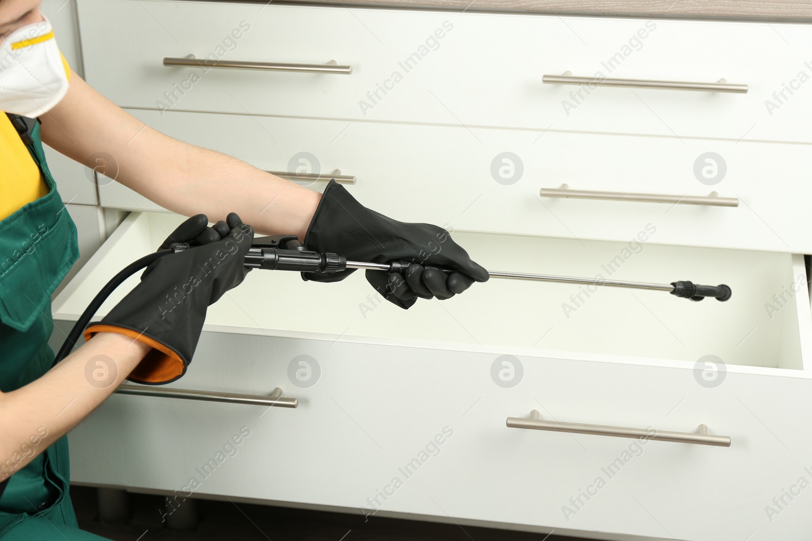 Photo of Pest control worker spraying pesticide on furniture indoors, closeup