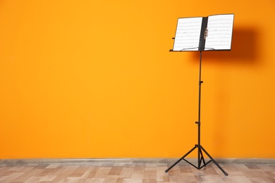 Photo of Note stand with music sheets near color wall indoors. Space for text