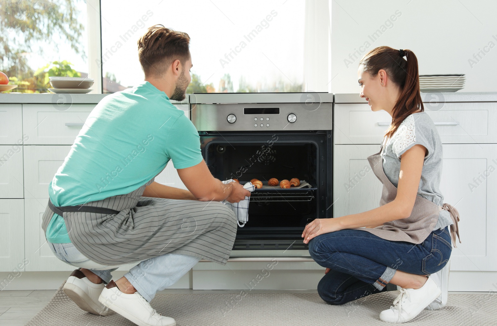 Photo of Young couple baking croissants in oven at home