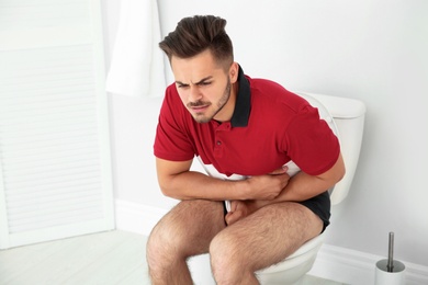 Young man suffering from diarrhea on toilet bowl at home