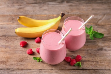 Photo of Glasses of tasty raspberry banana smoothie on wooden table