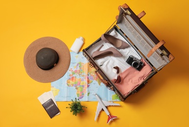 Photo of Flat lay composition with packed suitcase and travel accessories on yellow background. Summer vacation