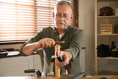 Photo of Man burnishing edges of leather belt in workshop