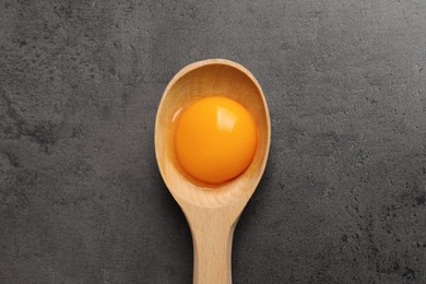 Photo of Wooden spoon with raw egg yolk on grey table, top view