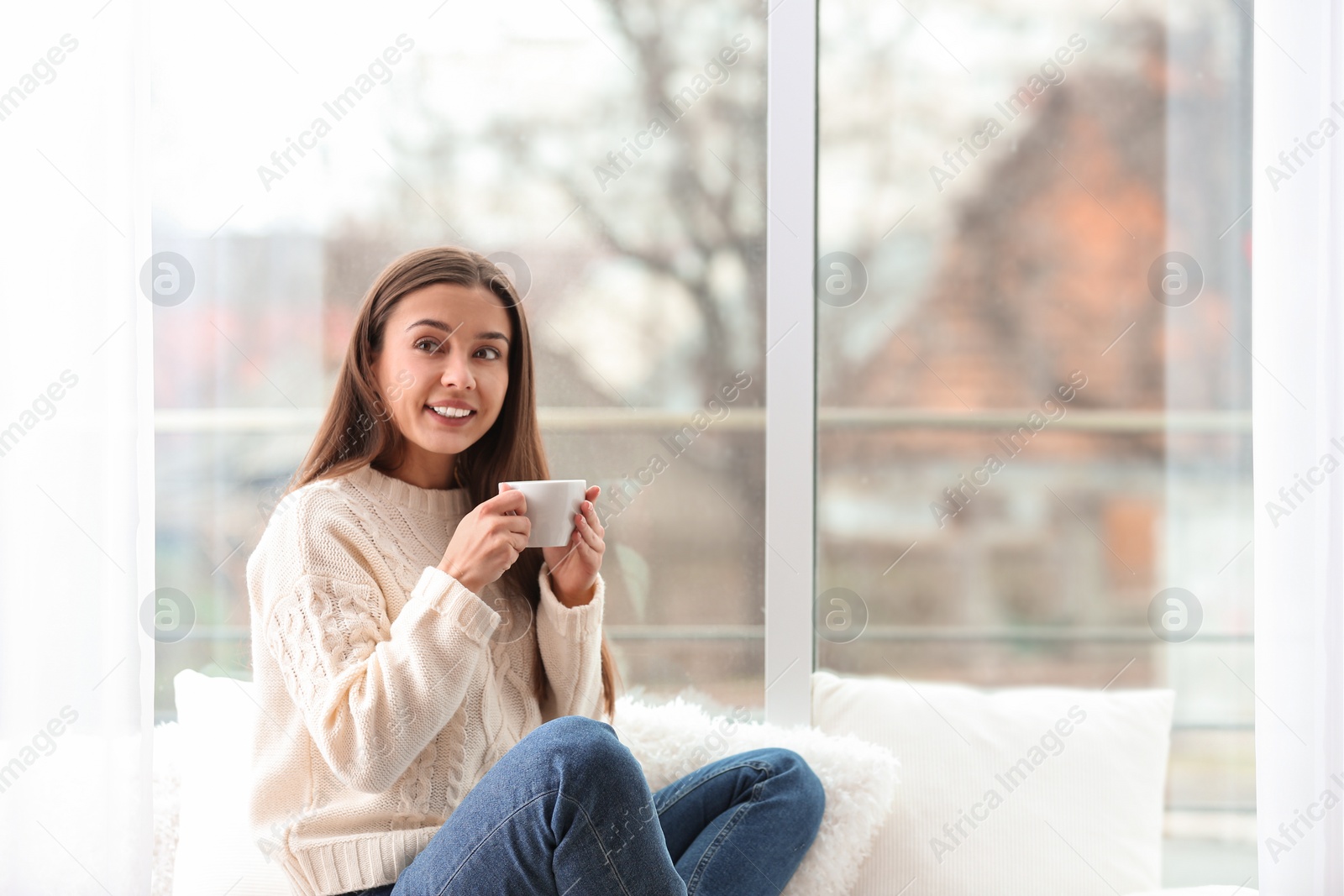 Young woman with cup near window indoors Photo of Young woman with cup near window indoors