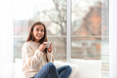 Photo of Young woman with cup near window indoors