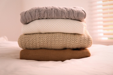 Photo of Stack of folded warm sweaters on bed indoors