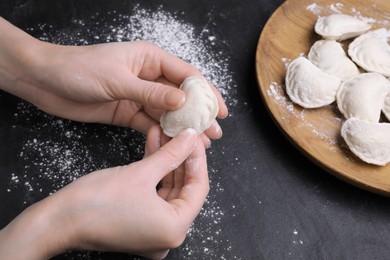 Photo of Woman making dumplings (varenyky) at black table, closeup