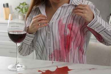 Photo of Woman with spilled wine over her shirt and marble table in kitchen, closeup