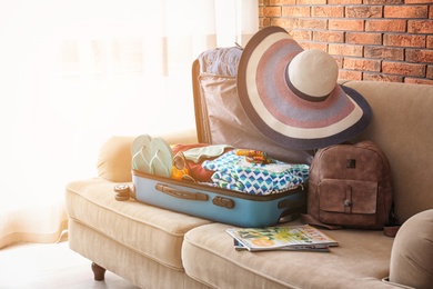 Photo of Open suitcase with different clothes and accessories on sofa indoors. Packing for vacation