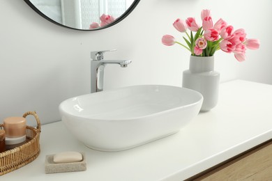 Photo of Vase with beautiful pink tulips and toiletries near sink in bathroom