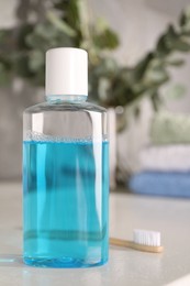 Photo of Bottle of mouthwash and toothbrush on white table in bathroom