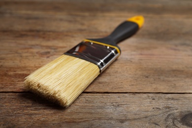 Photo of New paint brush on wooden table, closeup. Space for text