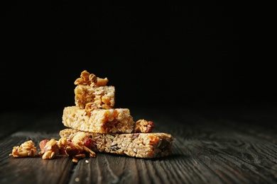 Photo of Different grain cereal bars on wooden table against black background. Healthy snack