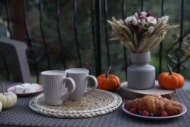 Photo of Snacking outdoors. Rattan table with cups of drink, croissants and autumn decor on terrace
