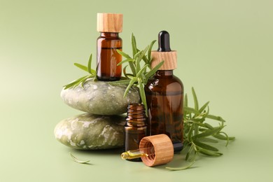 Photo of Aromatic essential oils in bottles, rosemary, pipette and pebble stones on green background