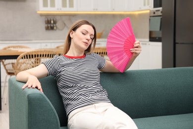 Photo of Woman waving pink hand fan to cool herself on sofa at home'
