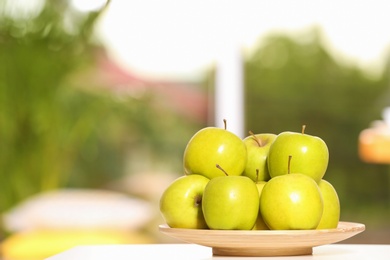 Photo of Plate with sweet green apples on table against blurred background, space for text