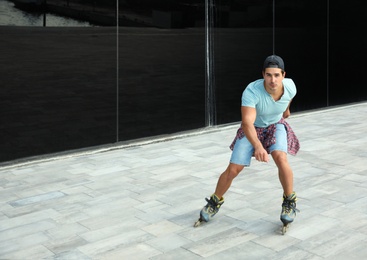 Photo of Handsome young man roller skating near glass building on city street, space for text