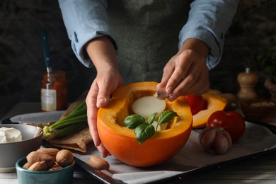 Photo of Woman stuffing pumpkin with vegetables at table, closeup