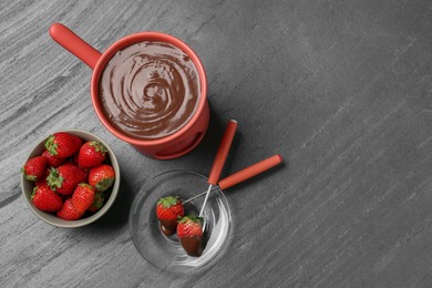 Photo of Fondue pot with melted chocolate, fresh strawberries and forks on grey table, flat lay. Space for text