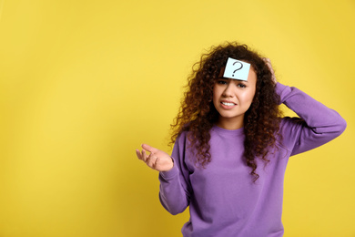 Photo of Emotional African-American woman with question mark sticker on forehead against yellow background. Space for text