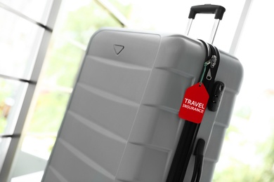 Photo of Stylish suitcase with travel insurance label on blurred background, closeup. Space for text