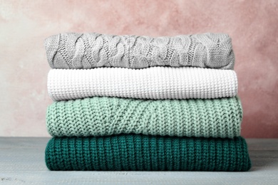 Photo of Stack of warm clothes on grey wooden table against light background. Autumn season