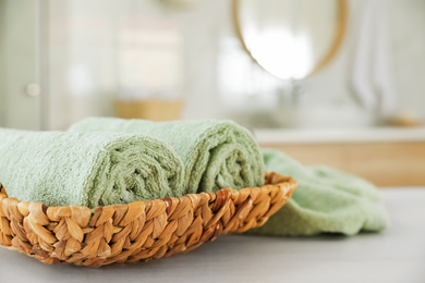Photo of Wicker basket with rolled towels on white wooden table in bathroom
