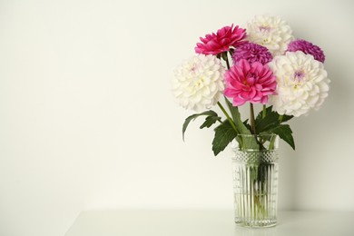Photo of Bouquet of beautiful Dahlia flowers in vase on table near white wall, space for text