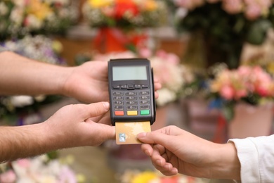 Photo of Woman using credit card for terminal payment in floral shop, closeup