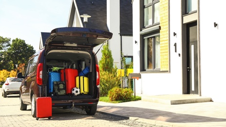 Photo of Car with suitcases in trunk near modern house outdoors. Moving day