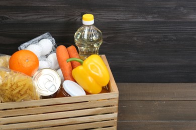 Crate with donation food on wooden table, closeup. Space for text