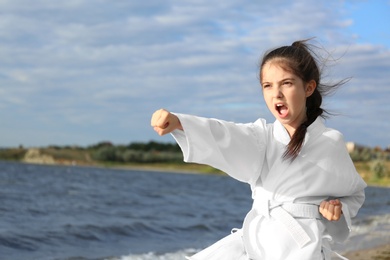 Photo of Cute little girl in kimono practicing karate near river