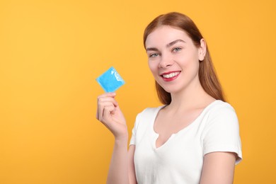 Photo of Woman holding condom on yellow background, space for text. Safe sex
