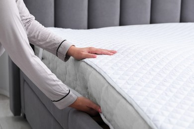 Photo of Woman putting new soft mattress on grey bed indoors, closeup