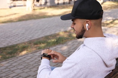 Photo of Young man with wireless headphones and smartwatch listening to music in park. Space for text
