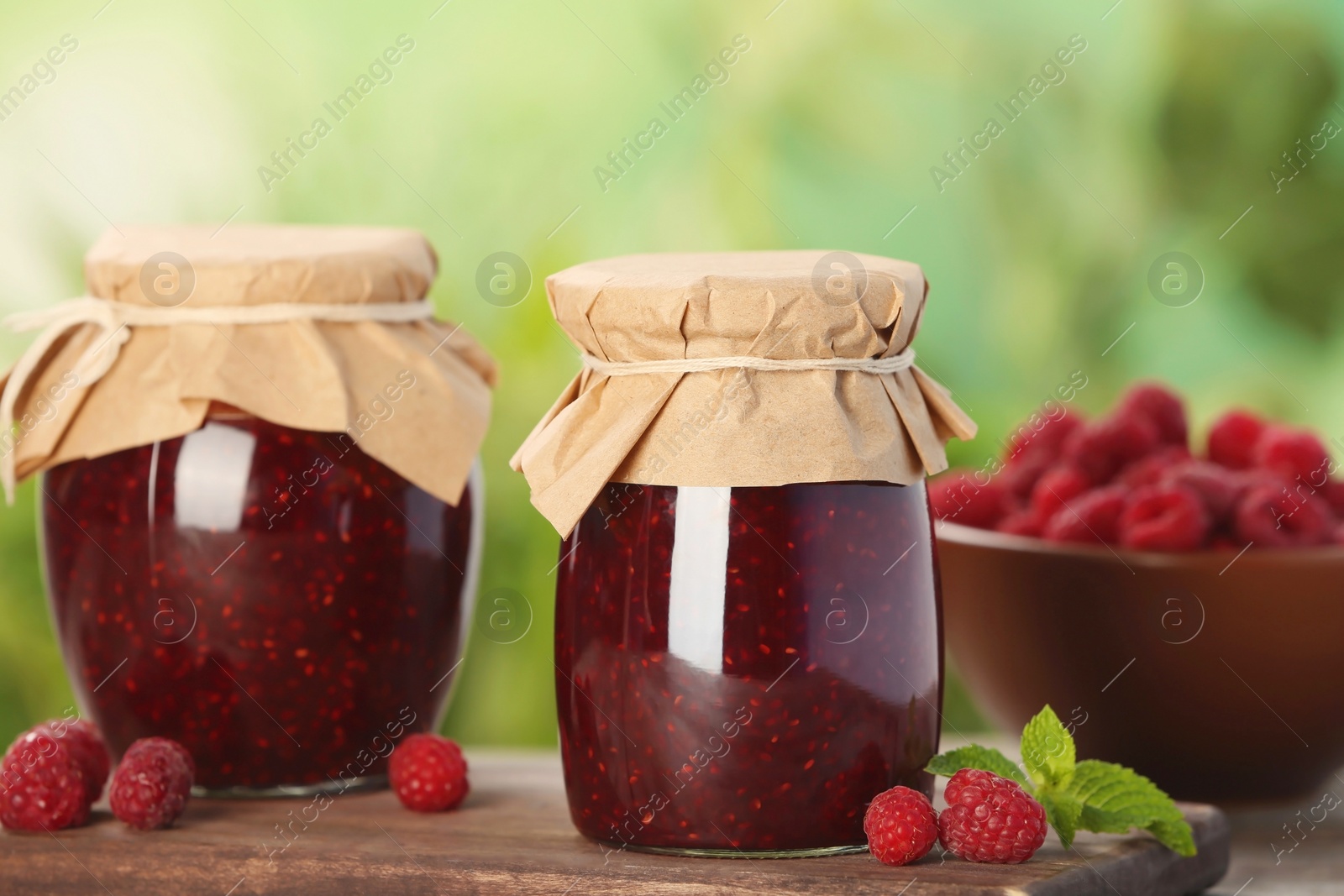 Photo of Jars with delicious raspberry jam on table against blurred background