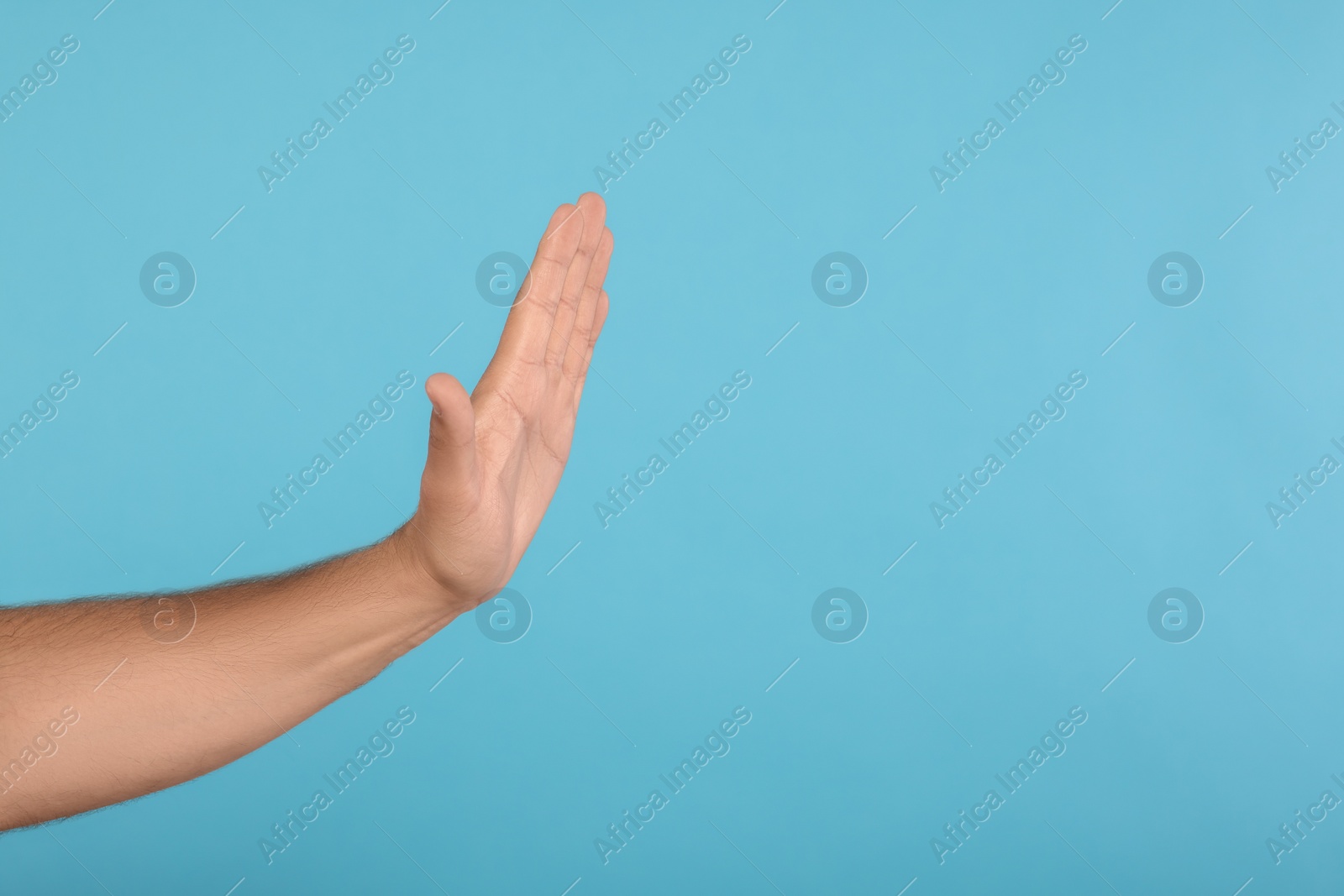Photo of Man showing stop gesture on light blue background, closeup with space for text