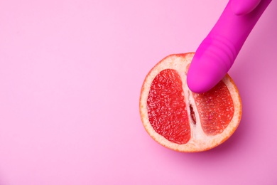 Photo of Half of grapefruit and purple vibrator on pink background, flat lay with space for text. Sex concept