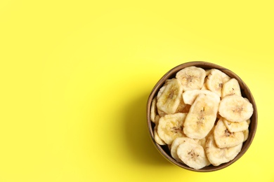 Photo of Wooden bowl with sweet banana slices on color background, top view with space for text. Dried fruit as healthy snack