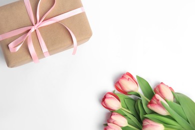 Photo of Beautiful gift box with bow and pink tulips on white background, flat lay. Space for text