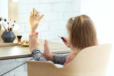 Photo of Cute little girl painting her nails in dressing room