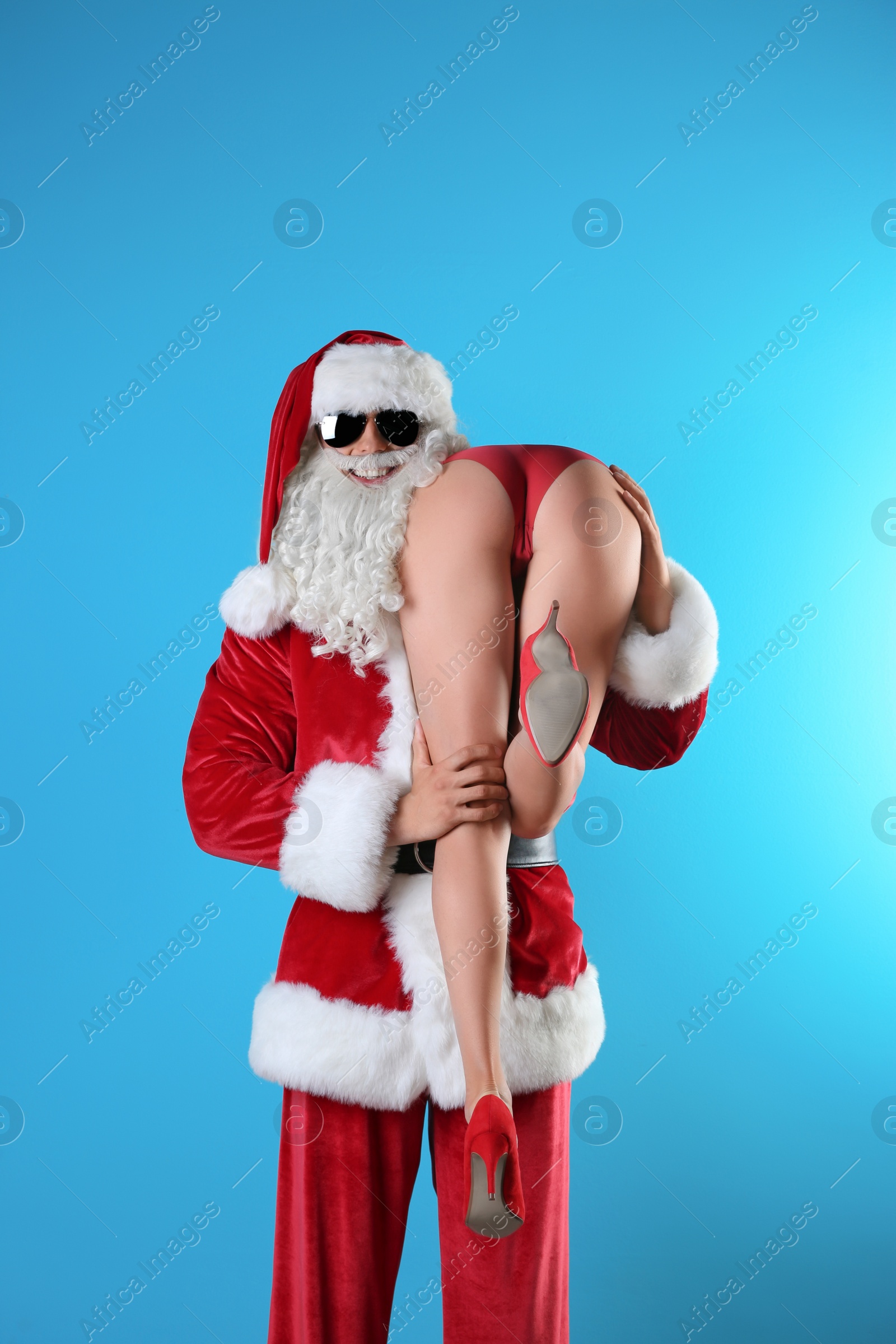 Young Santa Claus holding sexy naked woman on color background Photo of Young Santa Claus holding sexy naked woman on color background